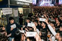 People holding and exchanging concert tickets at a crowded entrance with a resell sign